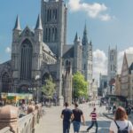 Pedestrians strolling on a sunny day near historic cathedral and buildings in a european city.