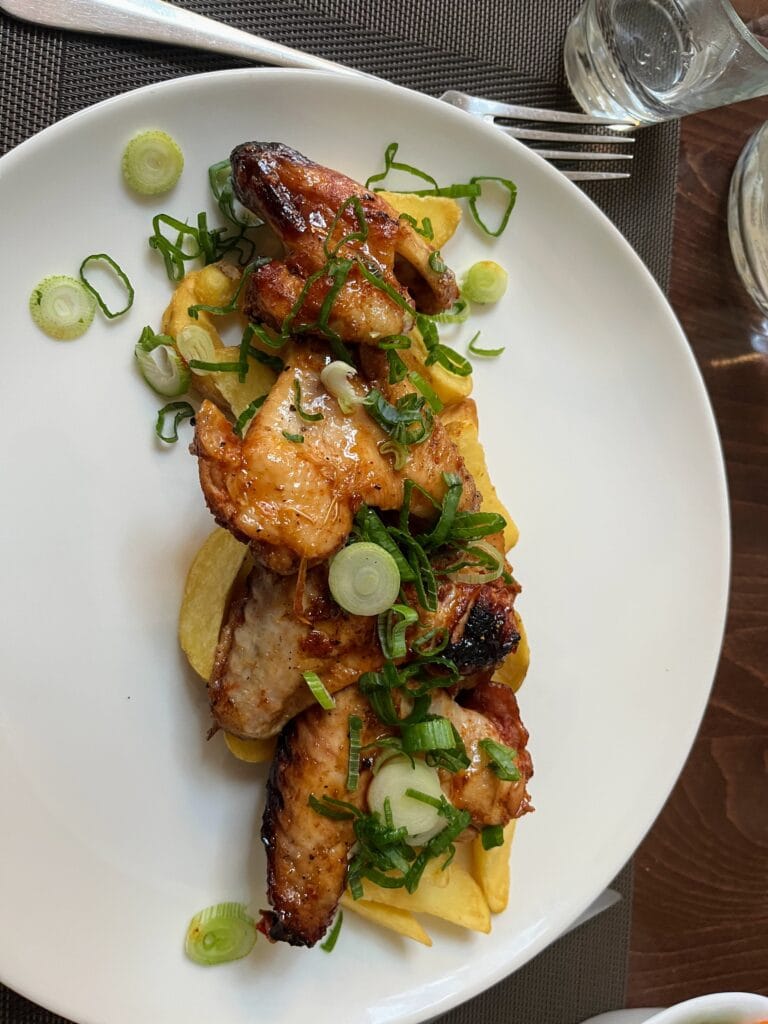A plate of roasted chicken wings garnished with sliced green onions, served over thick-cut potato fries.