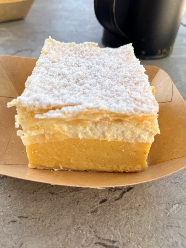 A slice of Bled cream cake with a layer of yellow custard, topped with whipped cream and a crispy pastry topping