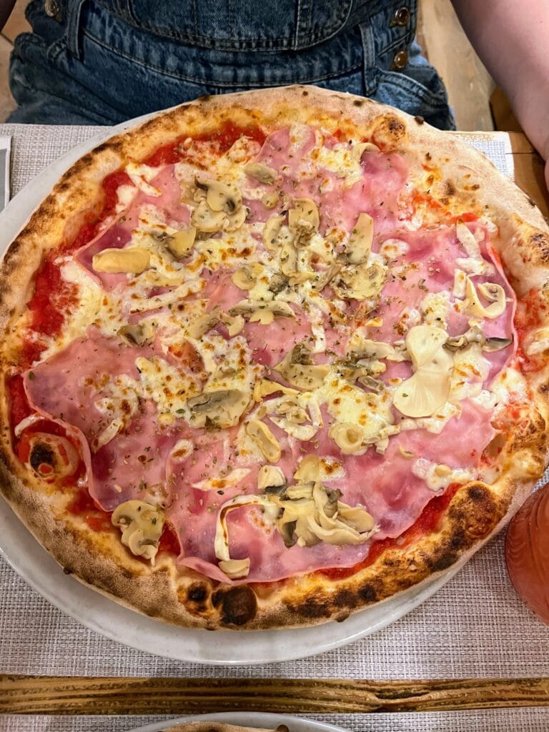 A freshly baked pizza topped with tomato sauce, melty cheese, ham, mushrooms, and artichokes served on a wooden table