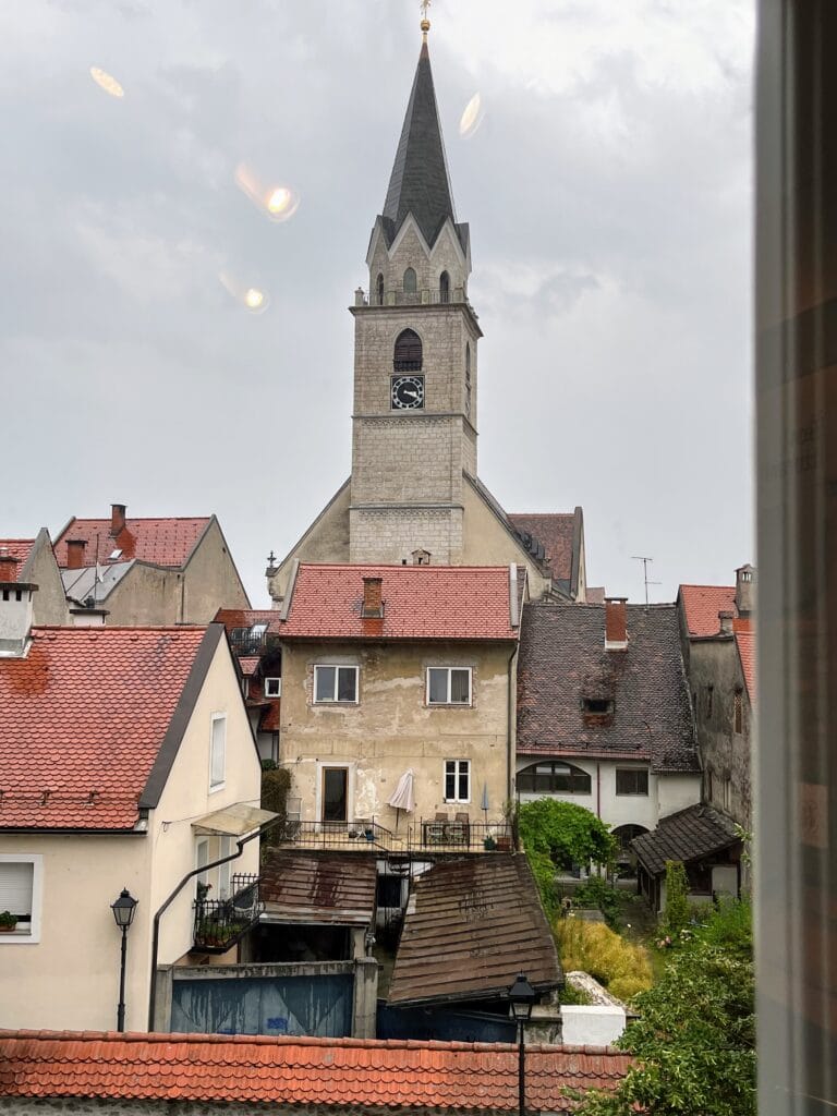 View of an old church tower rising above surrounding buildings on an overcast day.