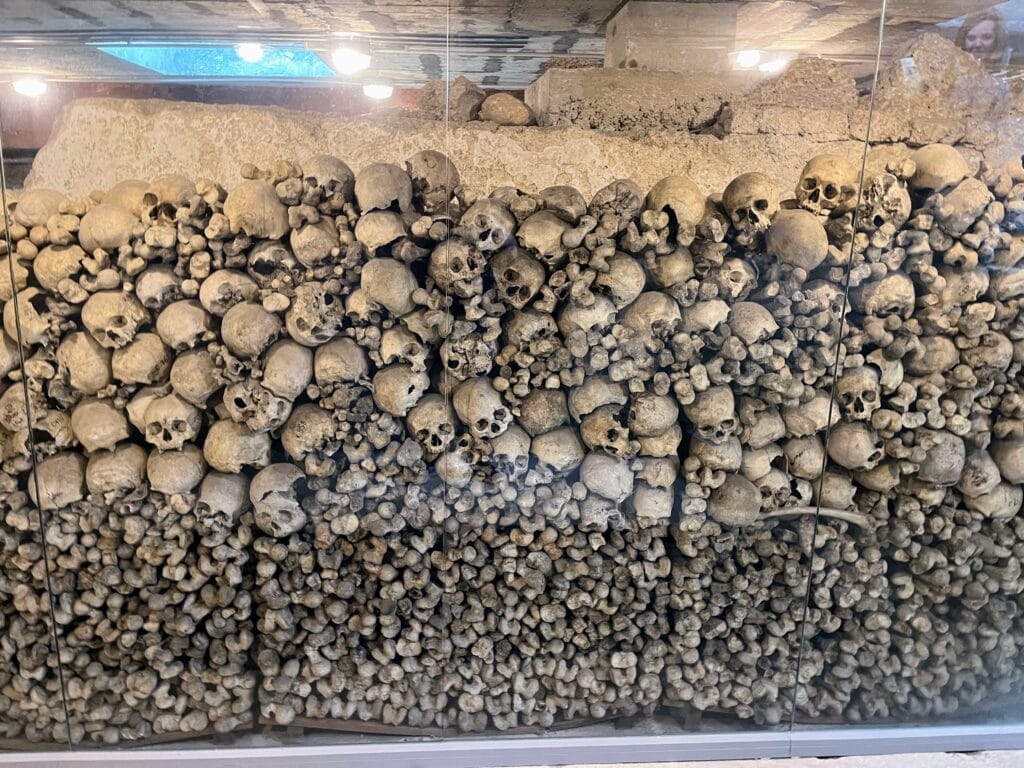 A historical ossuary containing numerous human skulls and bones displayed behind glass.