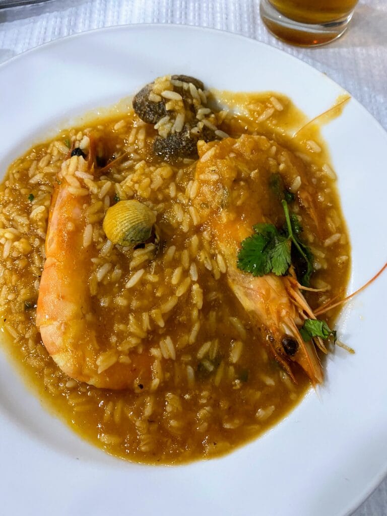 A plate of seafood risotto with a large shrimp, rice, and various shellfish, garnished with parsley.
