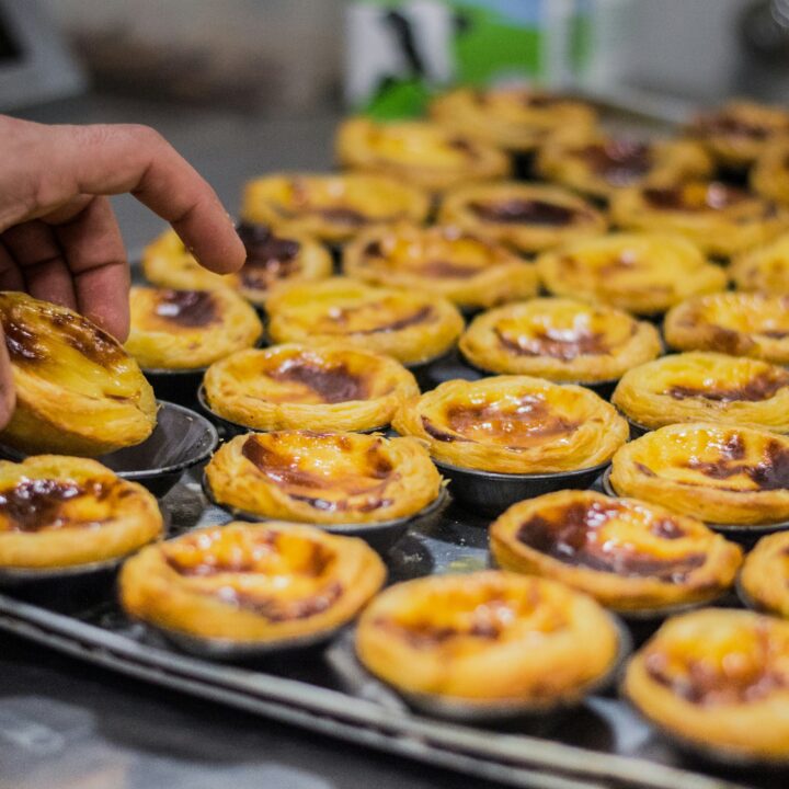 A person selecting a freshly baked pastel de nata from a tray full of portuguese custard tarts.