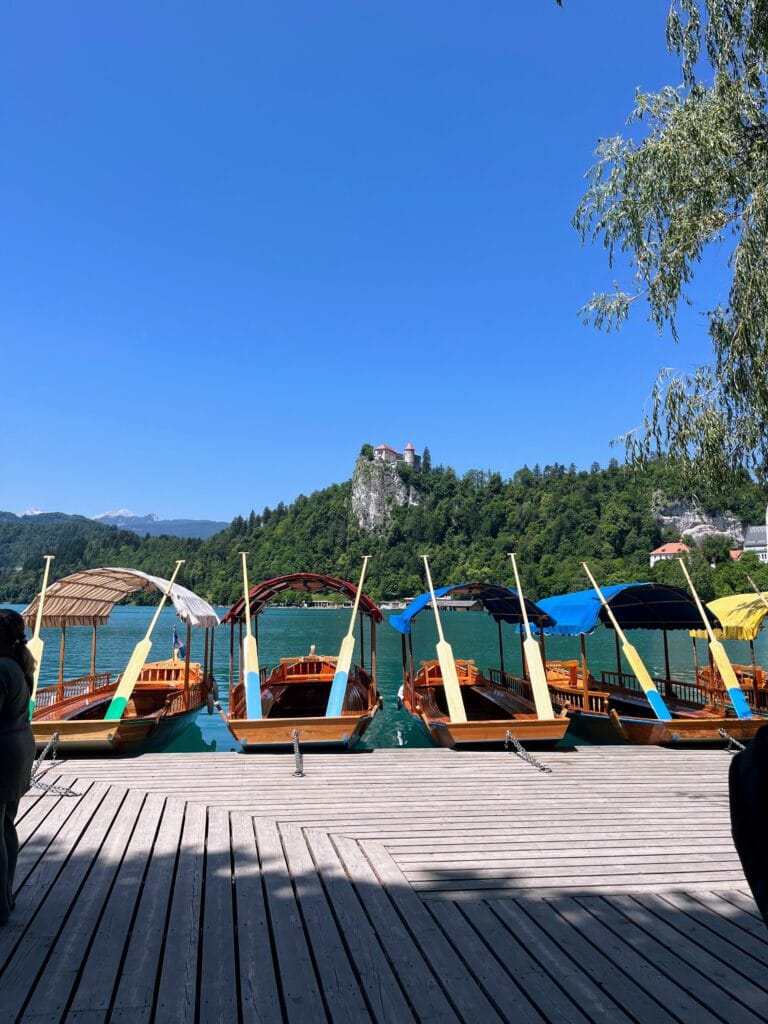 Traditional wooden boats moored at a lakeside against a backdrop of a castle atop a hill under clear blue skies.
