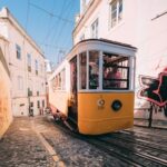 Vintage tram on a narrow cobbled street with passengers on board.