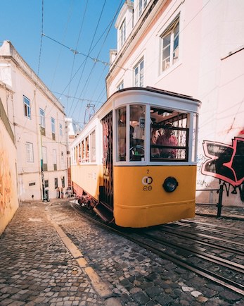 Vintage tram on a narrow cobbled street with passengers on board.