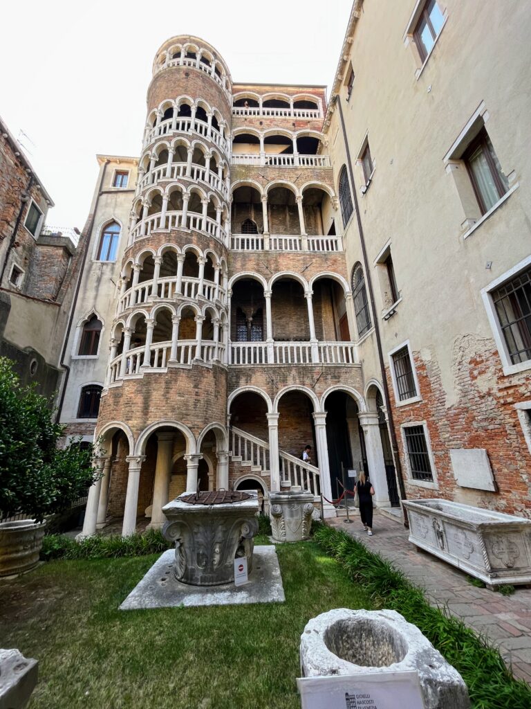 A historic spiral staircase attached to a larger building with a small grass courtyard