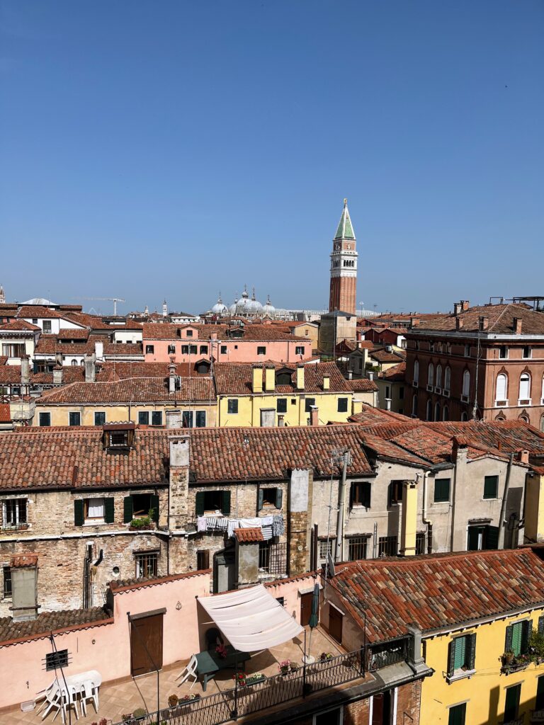 A view over a historic European city skyline with red roofs and a tall bell tower in the distance