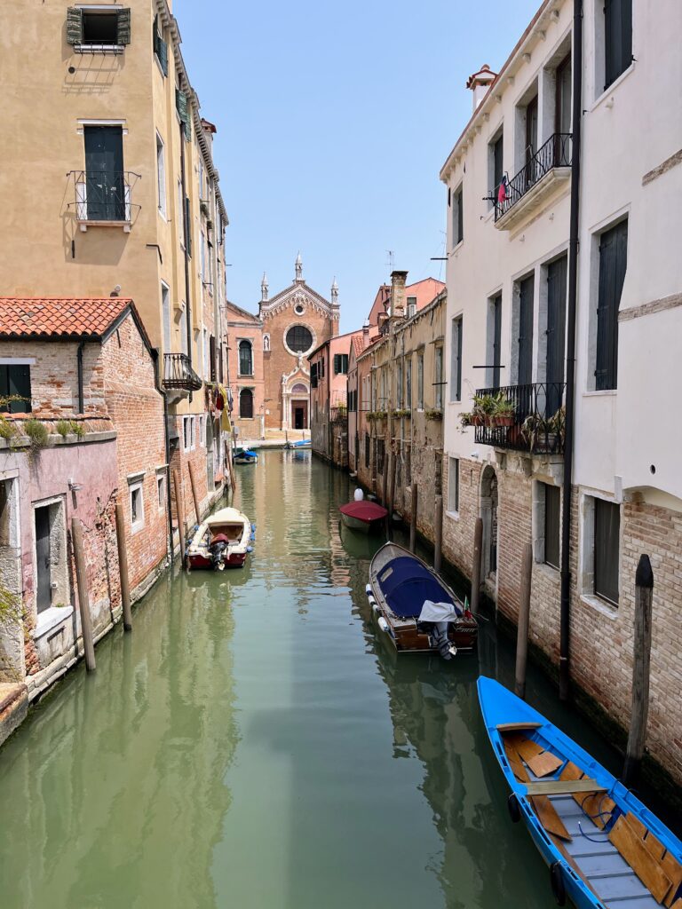 A calm canal with parked boats and historic buildings on both sides and a view of a church in the distance