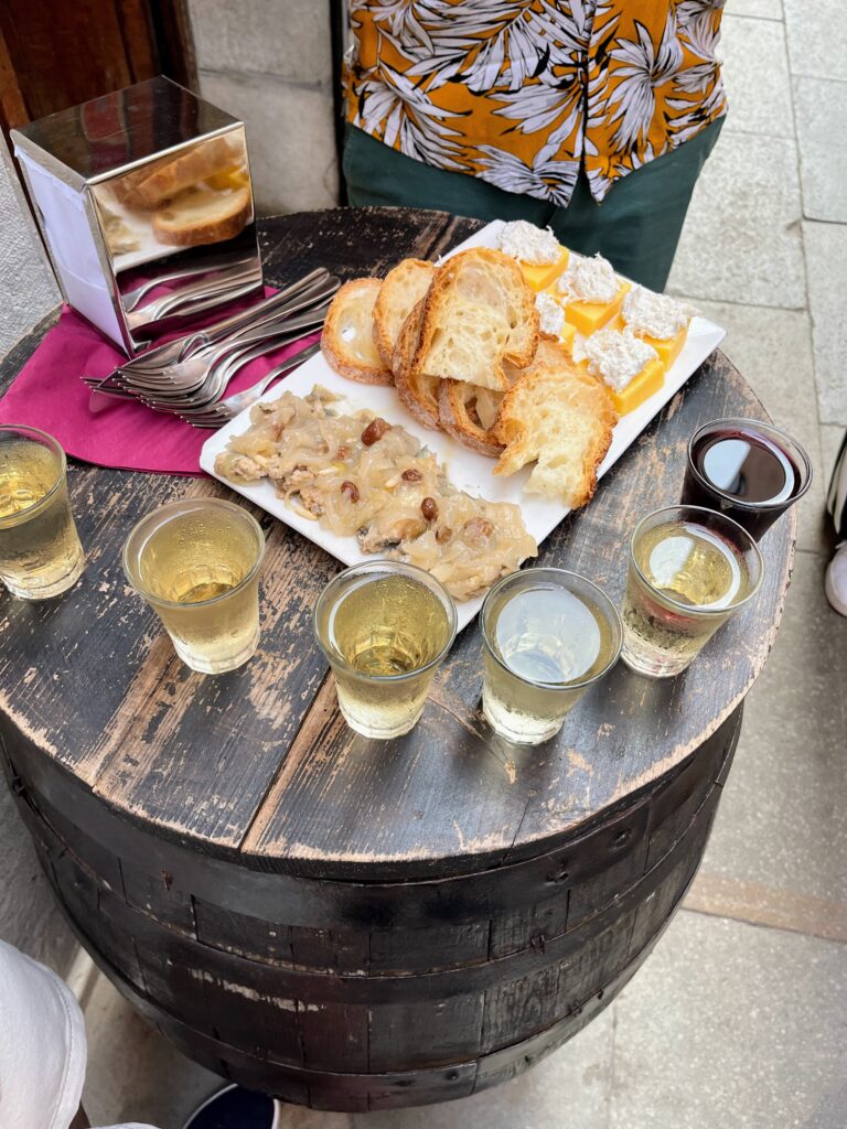 A plate of bread and food along with several cups of wine placed on top of an old wooden barrel