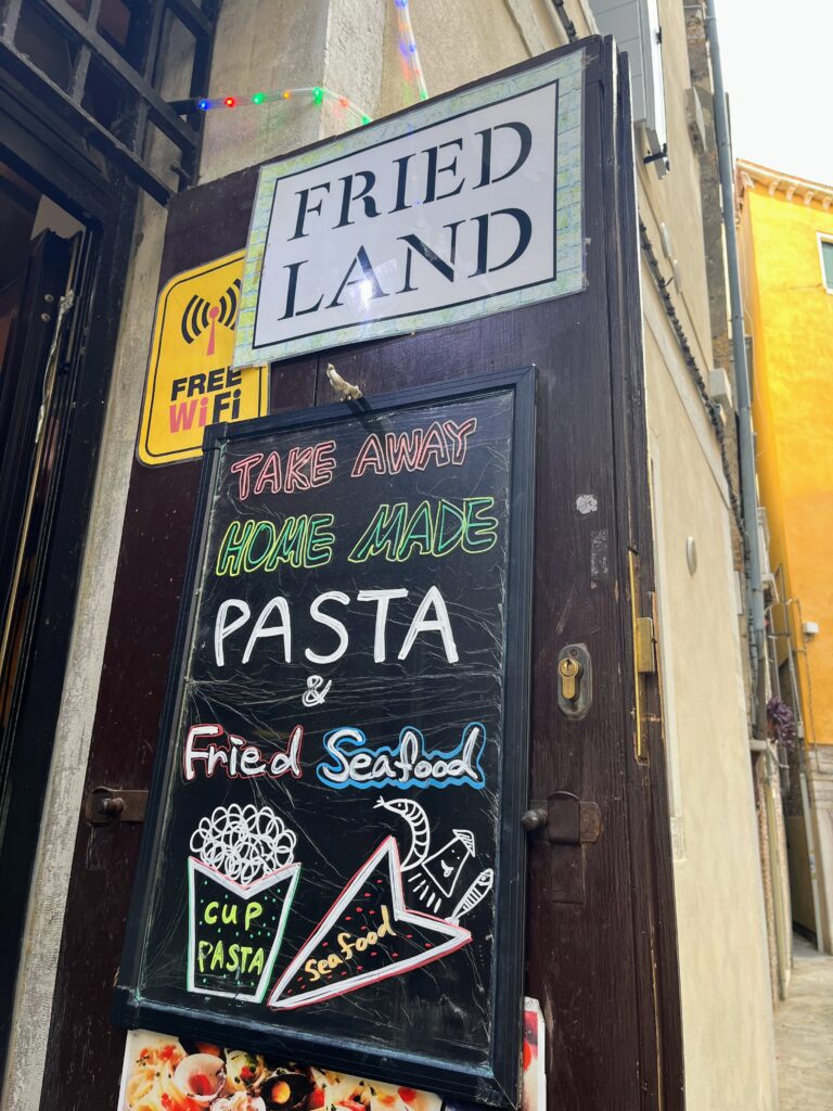 A sign outside a restaurant called Fried Land advertising pasta and fried seafood