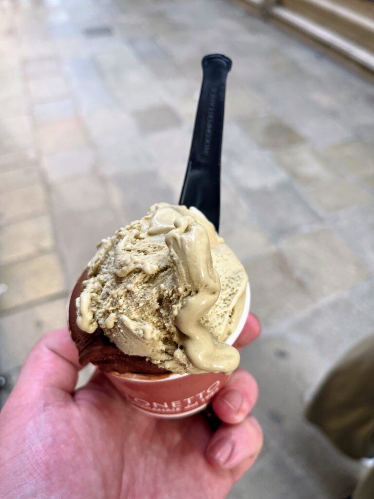 A cup of pale green and dark brown gelato with a black spoon