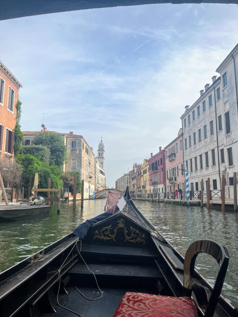 A view from a boat on a canal with historic buildings on either side and the end of the boat in the center of the frame