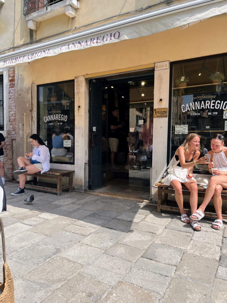 Picture of the outside of an Italian cafe called Torregazione Cannaregio with people outside sitting on benches.